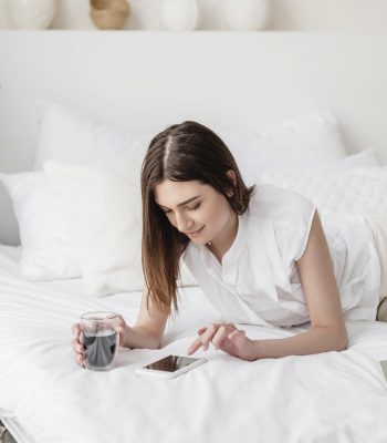 lady laying on her bed with cup of coffee scrolling on her phone