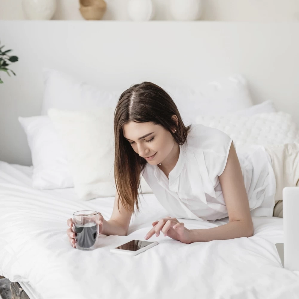 how to schedule your pinterest posts for free 1 lady laying on her bed with cup of coffee scrolling on her phone