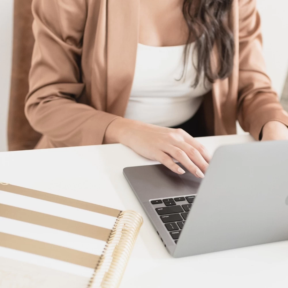 lady with brown blazer sitting at desk with laptop