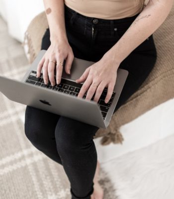 blogger sitting on the edge of the bed typing on a laptop