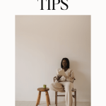 woman in a neutral track suit sitting on a wicker chair reading a book