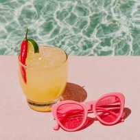 A retro-inspired lifestyle background image of a spicy margarita beside a pair of bright red sunglasses and a single chili pepper on a sunlit blue poolside surface. Negative space in the center of the image for text. Hard sunlight creates dramatic shadows and bright reflections. The image is minimal with large negative space and a playful editorial mood inspired by Palm Springs, Mexico City boutiques, and modern tequila campaigns. --ar 3:4 --profile 3uxkzbn --v 7 Job ID: ae984190-dc2f-42ee-9966-9ee02e77b0b9