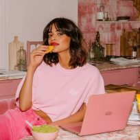 A soft candid portrait of a stylish founder sitting at a kitchen counter eating chips and guacamole while reviewing business notes and laughing at something on her phone. Warm sunlight creates natural shadows across the counter while pink and citrus tones subtly carry through the environment. The scene feels lived-in, charming, relatable, and stylishly imperfect. --ar 4:3 --profile 3uxkzbn --oref https://s.mj.run/Fr4AikQ14ww --ow 200 --v 7 Job ID: 5fcd458a-cf01-4779-8202-7733751b5148